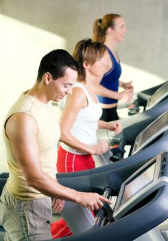 Three people on the treadmill in a gym, one choosing the program on the machine