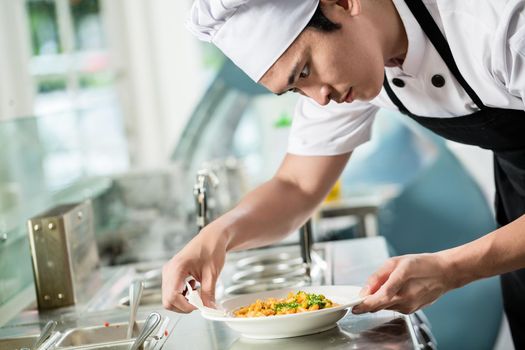 Gourmet chef plating up a dish of food in an Asian restaurant carefully wiping the sides of the plate for spillage