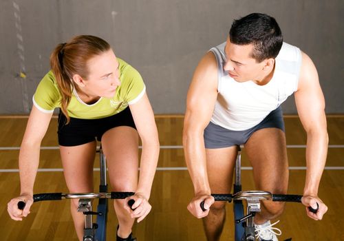 Couple using bikes in a fitness club, looking at each other competitively
