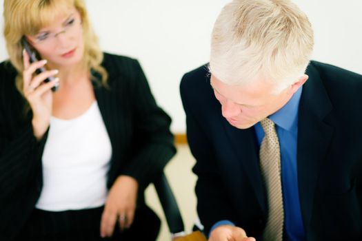 Man doing office work, woman using phone in the background (shallow depth of field, focus on eyes of man)