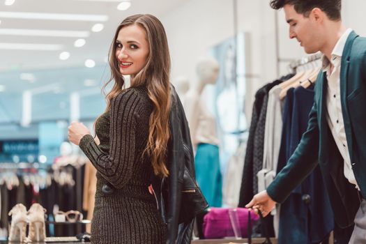 Woman trying a new leather jacket in hip fashion boutique showing it to her man