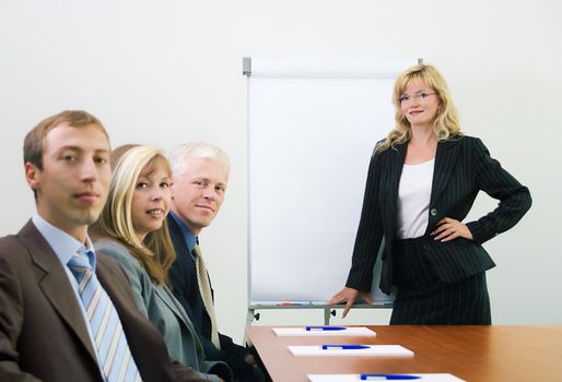 A group of people at a presentation held by a blond woman, looking at the viewer