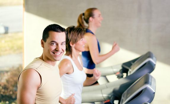 Three people on the treadmill in a gym, young man I front smiling