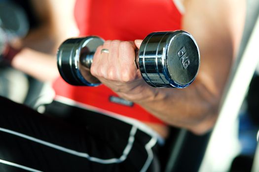 Woman lifting hand weights in a gym, focus on hand of woman and front of dumbbell