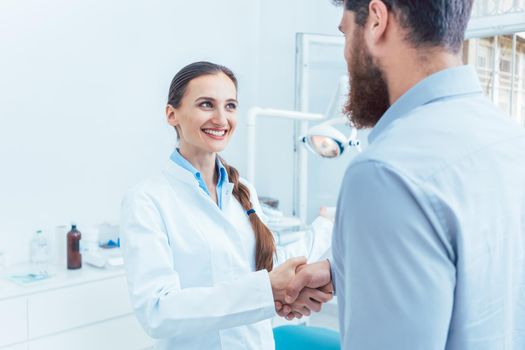 Portrait of a reliable and cheerful female dentist or dental surgeon shaking the hand of a patient in the dental office of a modern clinic
