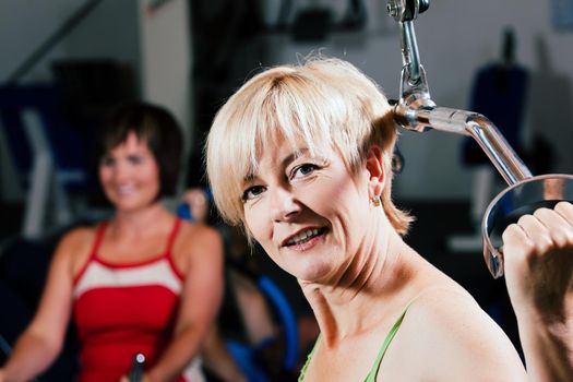 Senior woman in the gym lifting weights on a lat pull machine, exercising