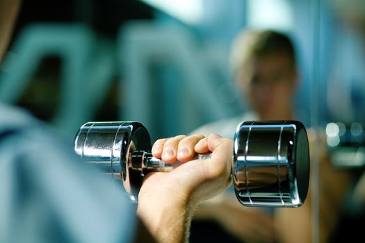 Young man with dumbbells, seeing himself in mirror (focus on dumbbells)