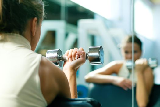 Woman lifting dumbbells in a gym, seeing herself in a mirror (focus only on the dumbbell)