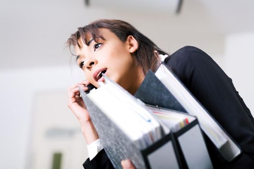 A female office employee carrying files and using cell phone simultaneously