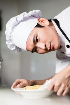 Asian chef plating up a bowl of food carefully wiping around the side to remove any spills, close up on his face with look of concentration