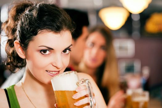 Group of three friends in a bar drinking beer - selective focus on beautiful woman in front zipping from her glass