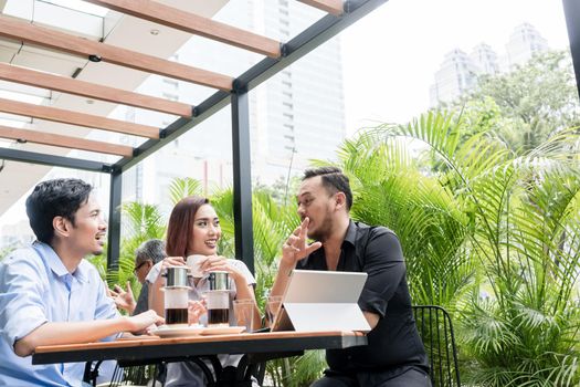 Delicious Vietnamese coffee served on the table of three young cheerful Asian friends outdoors in a modern cafeteria