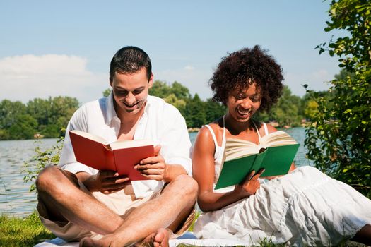 Couple reading books in the sunshine sitting at lake in summerCouple reading books in the sunshine sitting at lake in summer