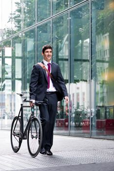 Businessman wheeling a bicycle through town along a pedestrian walkway as he commutes to work using eco-friendly transport