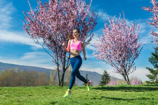 Woman doing sport running on hill between cherry trees blossoming