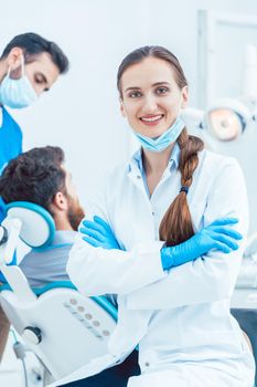 Portrait of a happy and confident female dentist wearing sterile white coat and surgical gloves, while looking at camera in the dental office of a modern clinic with reliable specialists