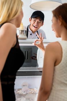 Young shop assistant laughing at a woman customer as she makes a perfect gesture with her hand as he weighs grated cheese