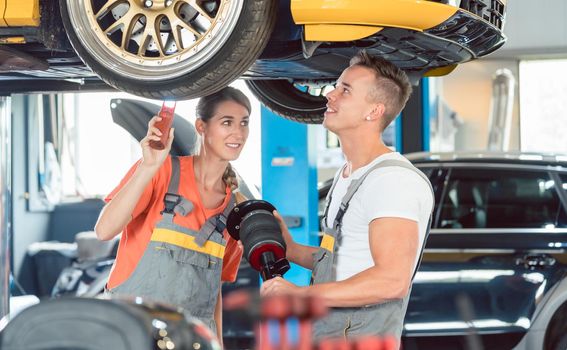 Experienced female auto mechanic checking tires before installing together with her colleague a new air suspension system in a modern automobile repair shop