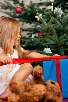 Cute Child with teddy bear toy finding her Christmas present in the morning still in her sleepwear and unwrapping it