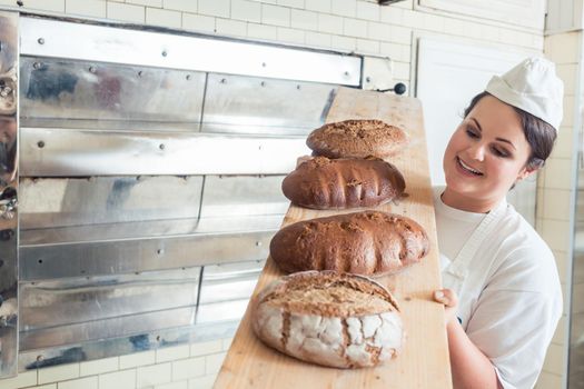 Baker woman presenting bread on board in bakery looking proudly into the camera