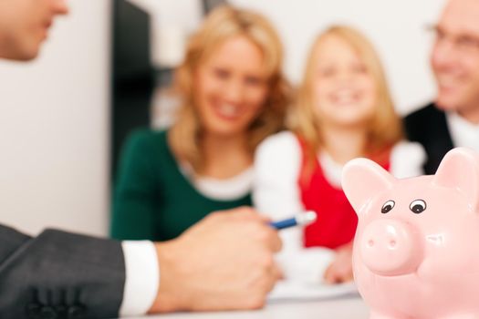 Family with their consultant (assets, money or similar) doing some financial planning - symbolized by a piggy bank in the front (focus only on piggy bank!)