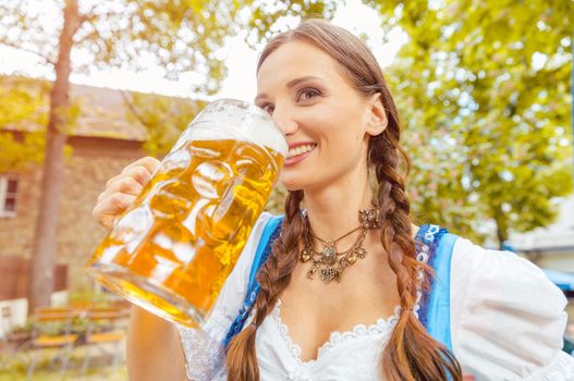 Woman wearing Dirndl is drinking beer in a Bavarian beer garden