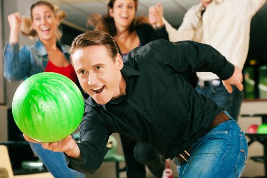 Group of four friends in a bowling alley having fun, three of them cheering the one in charge to throw the ball