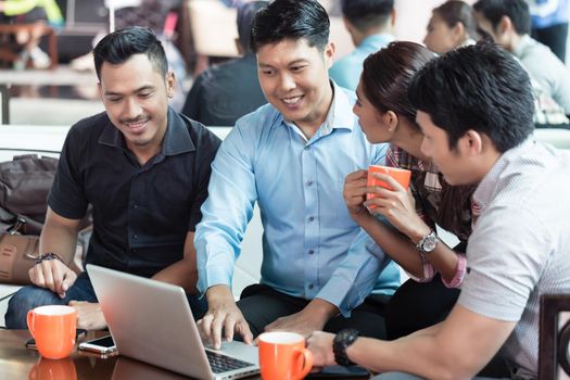 Team of four dedicated employees sitting in front of a laptop while working together at an innovative business project in a modern office