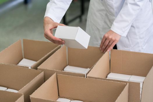 High-angle close-up view of the hands of a manufacturing worker putting packed products in cardboard boxes, before export or shipping during manual work in a cosmetics factory