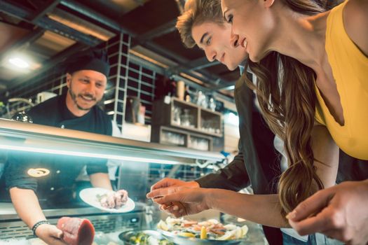 Experienced chef choosing raw seafood from the freezer for two customers in a trendy restaurant or cafeteria with fresh food