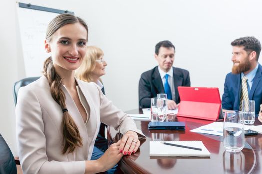 Portrait of a beautiful business woman looking at camera with a can-do attitude, while sitting down at a round table during a decision-making meeting with the board of directors