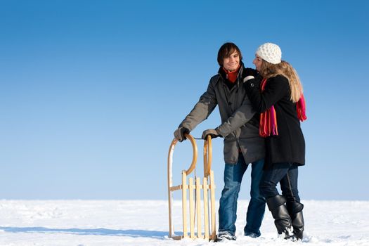 Happy couple in winter with sled in the snow