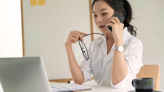 Young female entrepreneur working laptop computer and talking mobile phone.