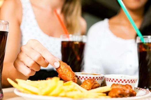 Two women - one is African American - eating chicken wings and drinking soda in a fast food diner; focus on the meal