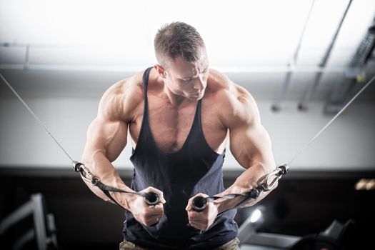 Bodybuilder doing butterfly on cable pull for better definition of his arm muscles