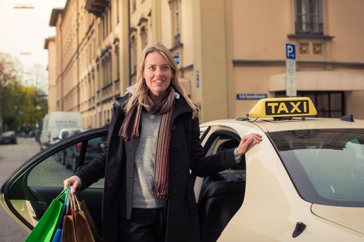 Young woman gets out of taxi carrying shopping bags in hands