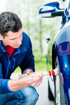 Man cleaning the alloy wheel hub of his car suing a soft bristle brush and soap to get between the spokes