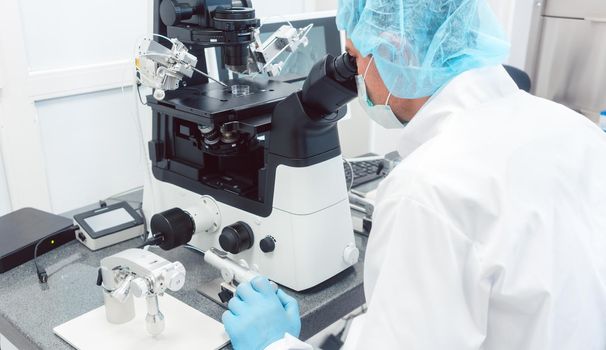Doctor or scientist looking thru microscope in biotech lab