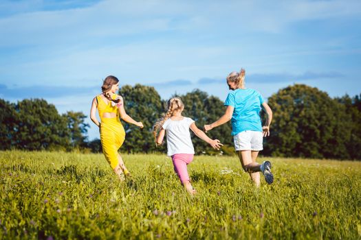 Two women and girl playful on a summer meadow running