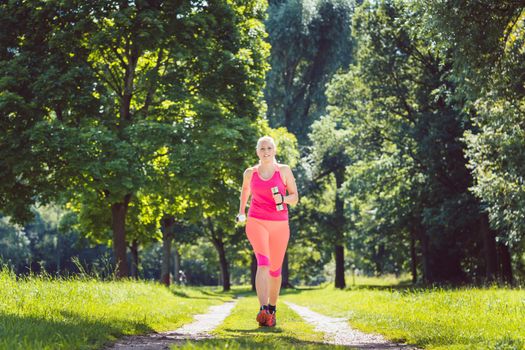 Woman running down a path on grass meadow with weight dumbbells