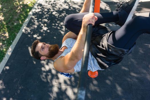 High-angle view of a strong and determined young man doing hanging oblique leg raises for abdominal muscles during street workout