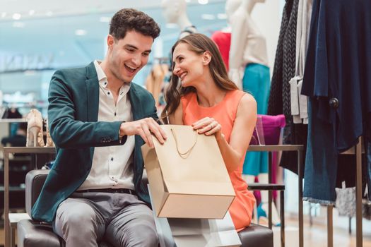Woman showing her man in shopping bag what she bought in fashion store