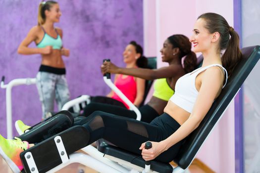 Side view of a beautiful woman smiling while exercising at the hip abductor machine during group workout at an exclusive fitness club for women