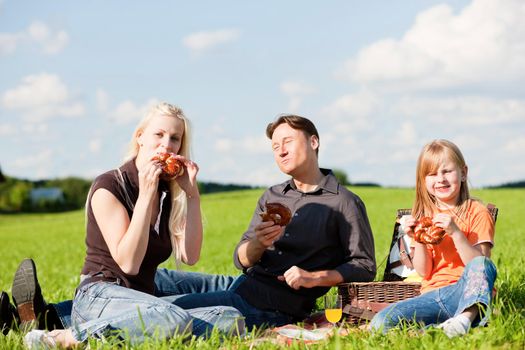 Family - father, mother and daughter child - having a picnic on a green meadow on a beautiful and bright summer day