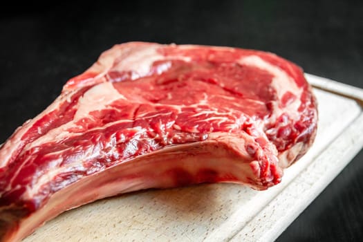 Raw beef prime rib on a cutting board isolated on black background