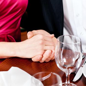 Couple, just hands to be seen, is holding hand while waiting for their food and drinks in a restaurant.