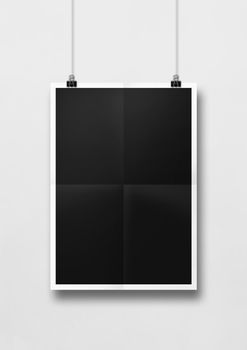 Black folded poster hanging on a white wall with clips. Blank mockup template