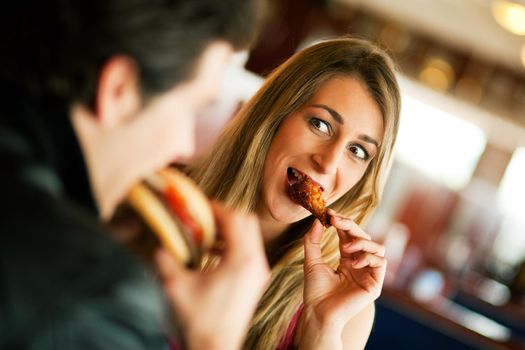 Couple in a restaurant or diner eating a hamburger and chicken wings flirting the while, shot with available light, very selective focus