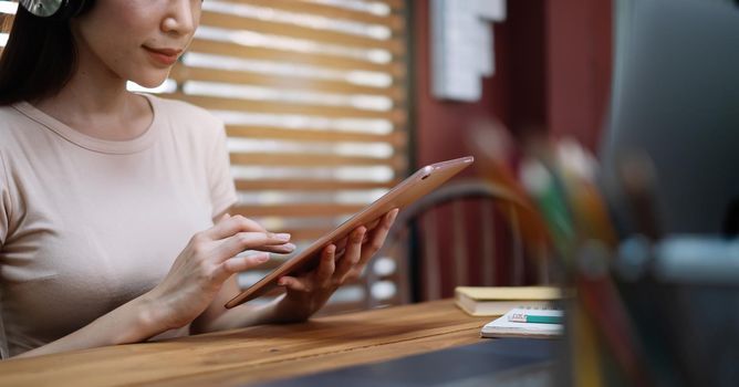 A asian female student sitting at the table, using tablet when studying online at home.