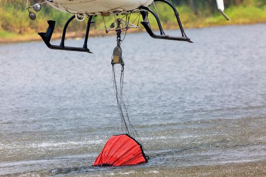 Firefighting helicopter refills water bucket in a pond